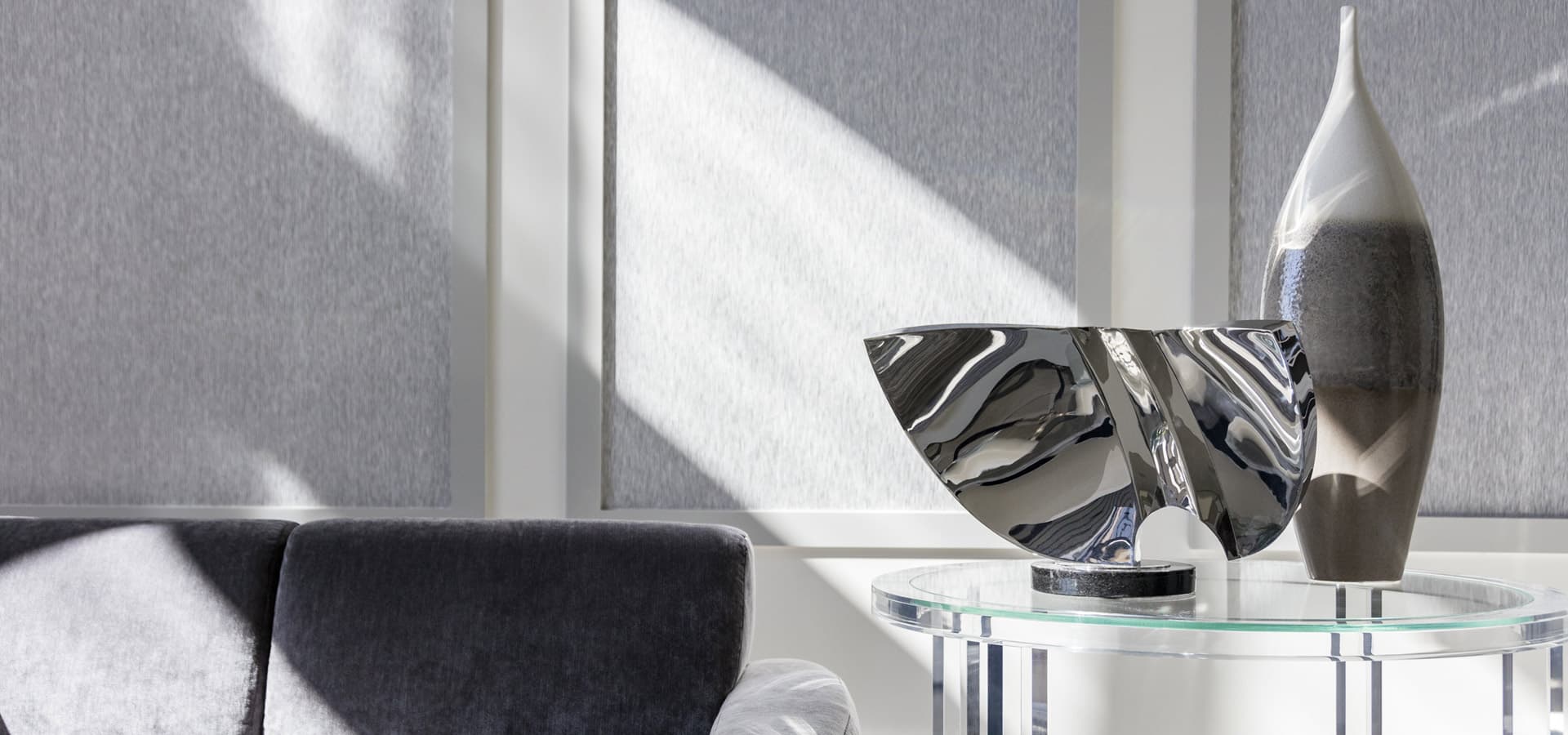Pirela Atelier Interiors.  Parkland, Florida. Luxurious monochromatic living room featuring a silver velvet sofa, modern geometric white coffee table, and textured gray wall panels.